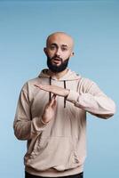 Young arab man taking break while showing time out gesture portrait. Person in casual hoodie clothes stopping communication with interruption signal and looking at camera photo