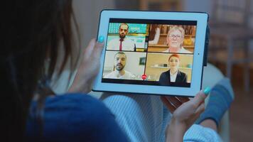 Woman listening online training on tablet late at night sitting on sofa. Remote worker having virtual meeting consulting with colleagues on videocall and webcam chat using internet technology. photo