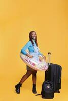 Tourist being excited about holiday trip, jumping in studio with inflatable and trolley bags. Female model preparing to travel abroad with suitcase, going on vacation journey. photo