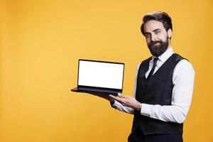 Confident person presents white screen on laptop, using modern pc to show isolated blank display on camera. Elegant restaurant personnel presenting empty mockup template in studio. photo
