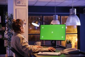 Businesswoman looking at green screen chroma key mock up computer with isolated display, working overtime at company strategy in startup office. Executive manager analyzing financial report growth photo