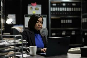 Professional asian accountant checking administrative analytical data on laptop in cabinet office surrounded by accountancy statistic reports. Businesswoman in file storage room photo