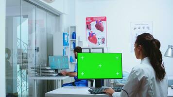 Doctor typing on computer with copy space in medicine hospital. Nurse working together with specialist medic. Computer with repleceable green screen used by medicine specialist in hospital and wearing uniform. photo