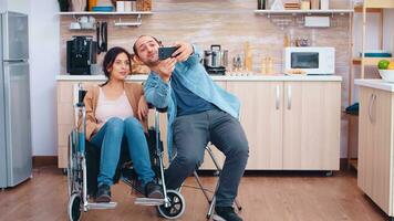 Boyfriend taking selfie with happy and disabled wife in wheelchair. Hopeful husband with handicapped disabled disability invalid paralysis handicap person next to him, helping her to reintegrate photo