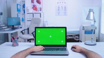 Pov of assistant using laptop with copy space available in hospital cabinet and doctor working on computer. Medic using notebook with chroma key on display in medical clinic. photo