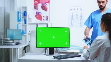 Nurse consulting with doctor in hospital cabinet while working on computer with copy space green screen available. Desktop with replaceable screen in medical clinic while doctor is checking patient radiography for diagnose. photo