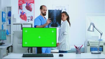 Monitor in hospital cabinet with chroma key while doctor and nurse checking x-ray image. Desktop with replaceable screen in medical clinic while doctor is checking patient radiography for diagnose. photo