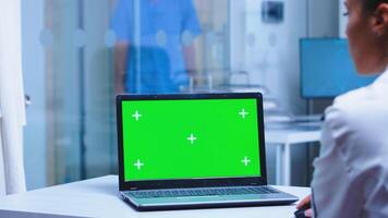 Over shoulder footage of doctor using laptop with copy space available in hospital . Nurse in uniform arriving in cabinet. Medic wearing uniform using notebook with chroma key on display in medical clinic. photo