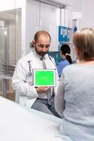 Doctor with green screen tablet in front of elderly patient explaining medical diagnosis. Ready chroma mockup for your app, text, video or other digital asset. photo