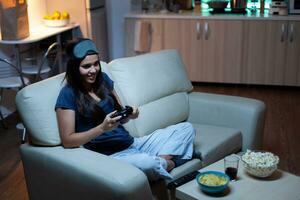 Woman sitting on sofa playing video games, smiling relaxing enjoying the evening. Excited determined gamer using controller joysticks keypad playstation gaming and having fun winning electronic game photo