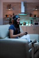 Gamer woman playing video games on console using controller and joysticks sitting on couch in front of TV. Excited determined person relaxing gaming with wireless controller having fun winning photo