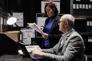 Business manager and consultant employee brainstorming accountancy market data analysis paperwork. Archival repository filled with cabinet, folders and graphic charts photo