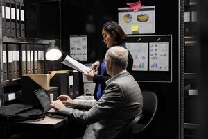 Businessmen executives discussing bureaucracy accountancy paperwork plan statistics document records. Archive file room filled with cabinet, folders and graphic flowcharts photo