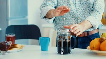 Older man making coffee using french press for breakfast in kitchen. Elderly person in the morning enjoying fresh brown cafe espresso cup caffeine from vintage mug, filter relax refreshment photo