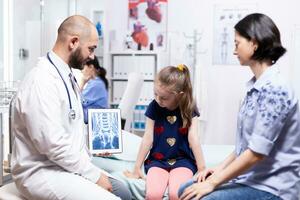 pediatra explicando radiografía para enfermo niño y madre en hospital oficina. cuidado de la salud médico especialista en medicina Proporcionar salud cuidado servicios tratamiento examen. foto