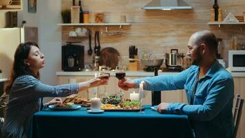 Young caucasian couple drinking a glass of wine during romantic dinner. Relax happy people clinking, sitting at table in kitchen, enjoying the meal, celebrating anniversary in the dining room photo