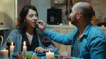 Happy funny couple in love eating grapes at dinner, smiling and having fun during romantic dinner. Wife and husband celebrating anniversary with red wine, tender moments at candle lights in kitchen photo