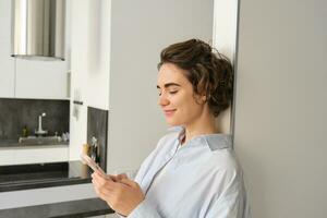 Portrait of brunette woman with smartphone, sending message, checking her mobile application, ordering delivery to home photo