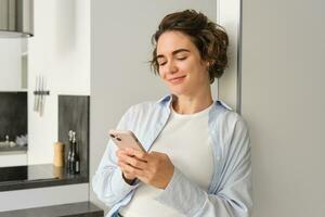 Portrait of brunette woman with smartphone, sending message, checking her mobile application, ordering delivery to home photo