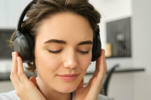 cerca arriba retrato de mujer rostro, escuchando a música en su inalámbrico auriculares con deleite y placer, disfrutando bueno sonido calidad en auriculares foto