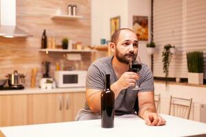 Man drinking alone at home because of loneliness and sadness. Unhappy person disease and anxiety feeling exhausted with having alcoholism problems. photo