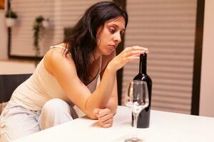 Sad lady drinking alone in the kitchen. Unhappy person suffering of migraine, depression, disease and anxiety feeling exhausted with dizziness symptoms having alcoholism problems. photo