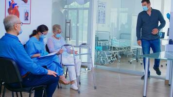 Nurse in hospital waiting room with face mask against covid19 helping invalid senior woman to fill documents. Doctor inviting old man in examination room. Health care system during global pandemic photo