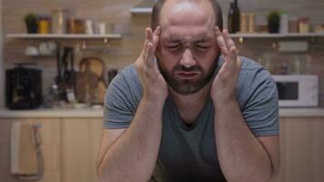 cerca arriba de hombre con dolores de cabeza sentado en el cocina. estresado cansado infeliz preocupado indispuesto ama de casa sufrimiento de migraña, depresión, enfermedad y ansiedad sensación agotado con mareo síntomas foto