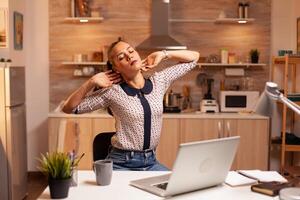 Freelance woman stretching arms because of exhaustion while working overtime from home. Employee using modern technology at midnight doing overtime for job, business, busy, career, network, lifestyle ,wireless. photo