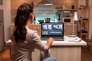 Back view of creative filmmaker working on a movie on laptop during midnight. Content creator in home working on montage of film using modern software for editing late at night. photo