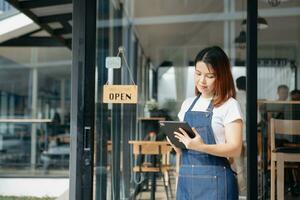 Young female hanging a welcome sign in front of a coffee shop. Beautiful waitress or hostess holding a tablet preparing  in a restaurant. photo