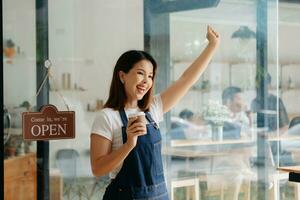 Young female hanging a welcome sign in front of a coffee shop. Beautiful waitress or hostess holding a tablet preparing  in a restaurant. photo