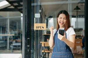 Young female hanging a welcome sign in front of a coffee shop. Beautiful waitress or hostess holding a tablet preparing  in a restaurant. photo