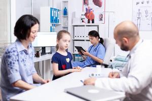 Nurse using tablet pc while doctor is consulting sick child in hospital office. photo