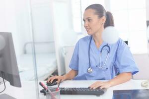 Medical practitioner using computer in hospital office. Health care physician using computer in modern clinic looking at monitor, medicine, profession, scrubs. photo