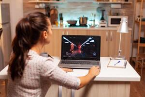 Female game developer working on new project on personal laptop in home kitchen during night time. Professional gamer playing online videop games on her personal computer. Geek cyber esport. photo