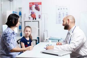 médico hablando acerca de tratamiento con madre de enfermo niño en hospital oficina. cuidado de la salud médico especialista en medicina Proporcionar salud cuidado servicios tratamiento examen. foto