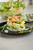 Layered salad of cabbage and other vegetables with pieces of red fish in a plate. photo