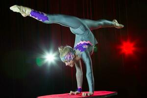 un niña con un flexible cuerpo. realiza un circo artista. circo gimnasta. equilibrio acto. el niño realiza un acrobático truco foto