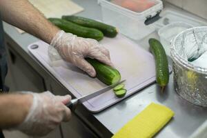 el cocinero cortes un Pepino con un Sushi o ensalada cuchillo. foto