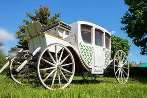 un antiguo blanco carro desde el decimonoveno siglo en un verde césped. el prototipo de un moderno coche. foto