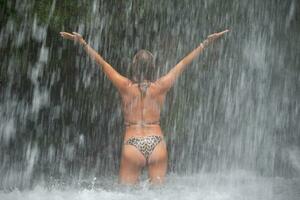 hermosa joven mujer relaja debajo un cascada. sexy niña en un bikini posando cerca un cascada en el zona tropical. foto