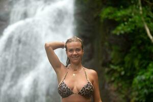 de cerca retrato de un hermosa niña con mojado pelo en contra el antecedentes de un cascada y tropical verdor. foto