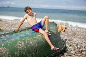 un chico en el playa se sienta en un antiguo bote. vacaciones a mar. foto