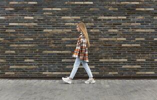 young woman walks down the street in front of a brick wall photo