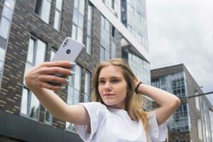 young woman taking a selfie or using a mirror app on the street against the backdrop of modern buildings photo