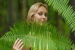 joven hermosa mujer entre el helecho hojas en el bosque foto