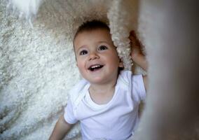 pequeño chico sonriente en pie en el antepecho por el ventana detrás el cortina foto