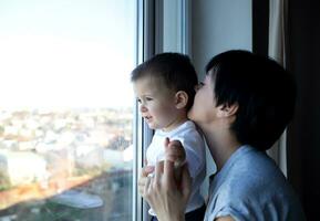 pequeño chico con su joven hermosa madre Mira fuera el ventana foto