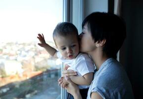 pequeño chico con su joven hermosa madre Mira fuera el ventana foto